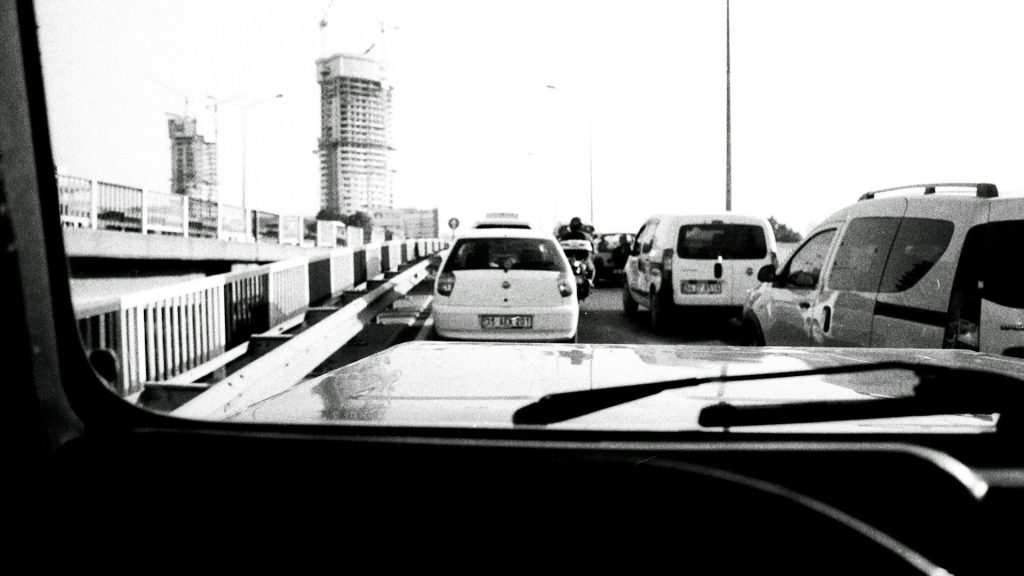 Beginnende bestuurders in file op brug, gezien vanuit de auto, met stadsverkeer op de achtergrond.